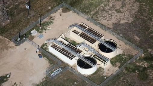 Aerial view of a water treatment facility with circular clarifier tanks and rectangular treatment beds